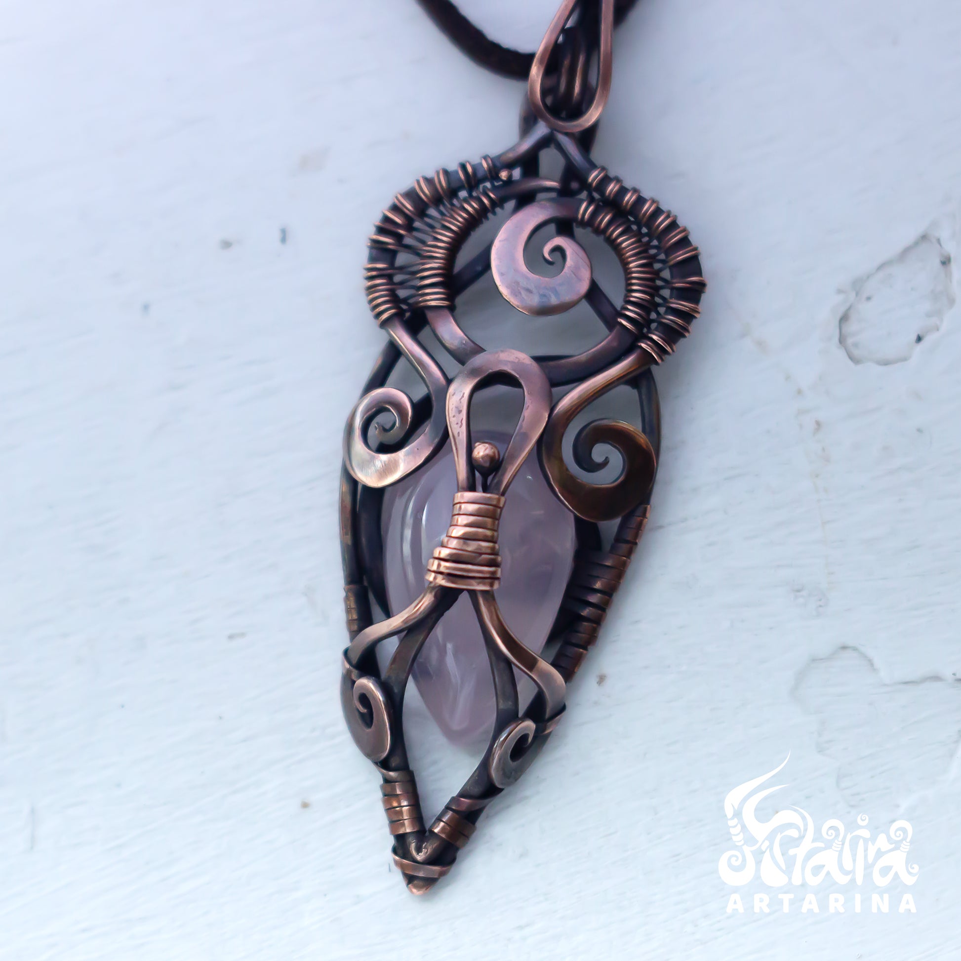 Copper wire-wrapped pendant with a central stone on a light gray background