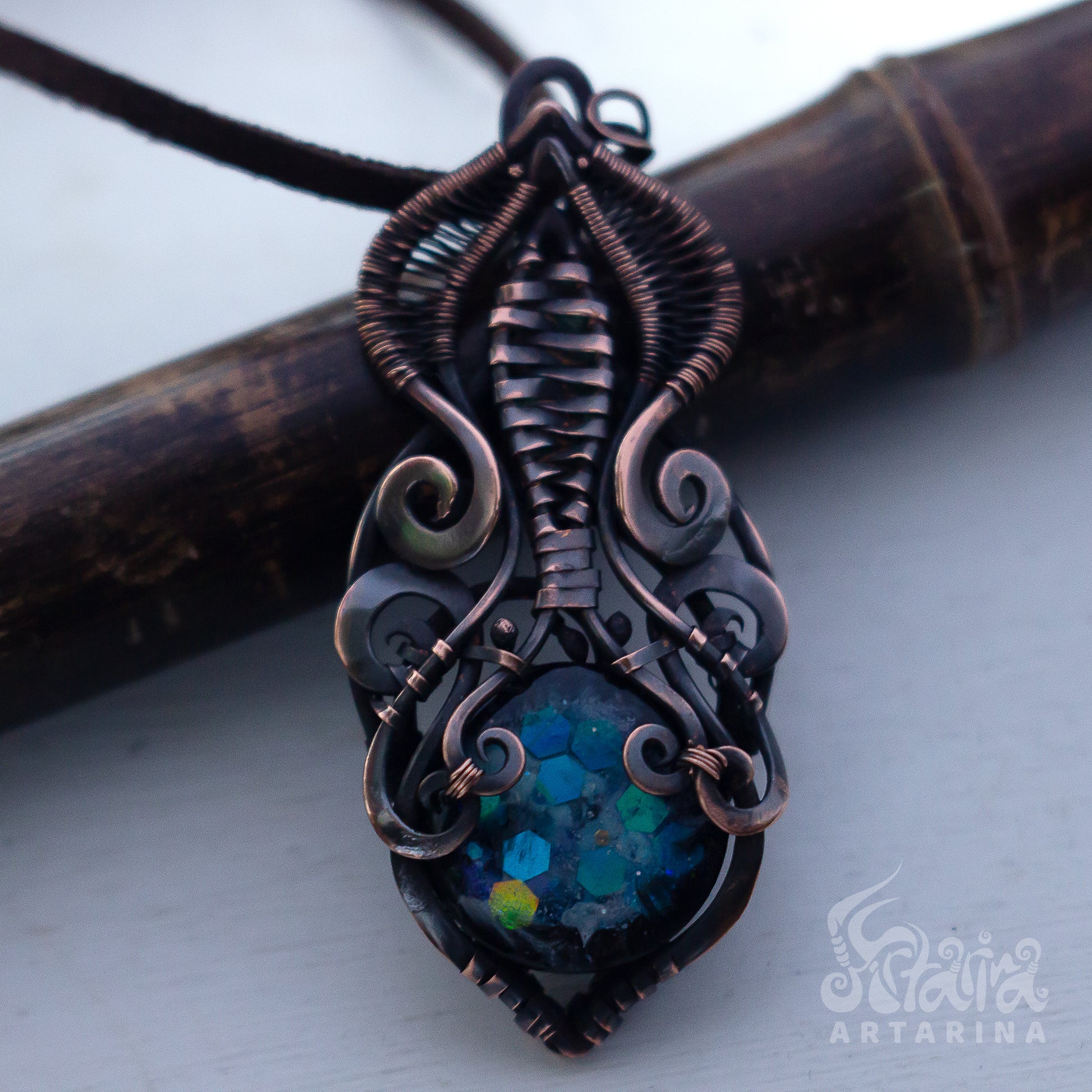 Ornate copper pendant with a blue gemstone on a white background