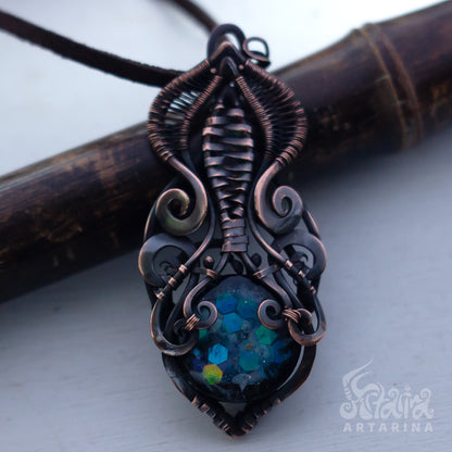 Ornate copper pendant with a blue gemstone on a white background