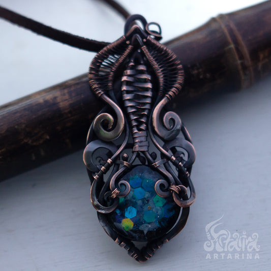 Ornate copper pendant with a blue gemstone on a white background