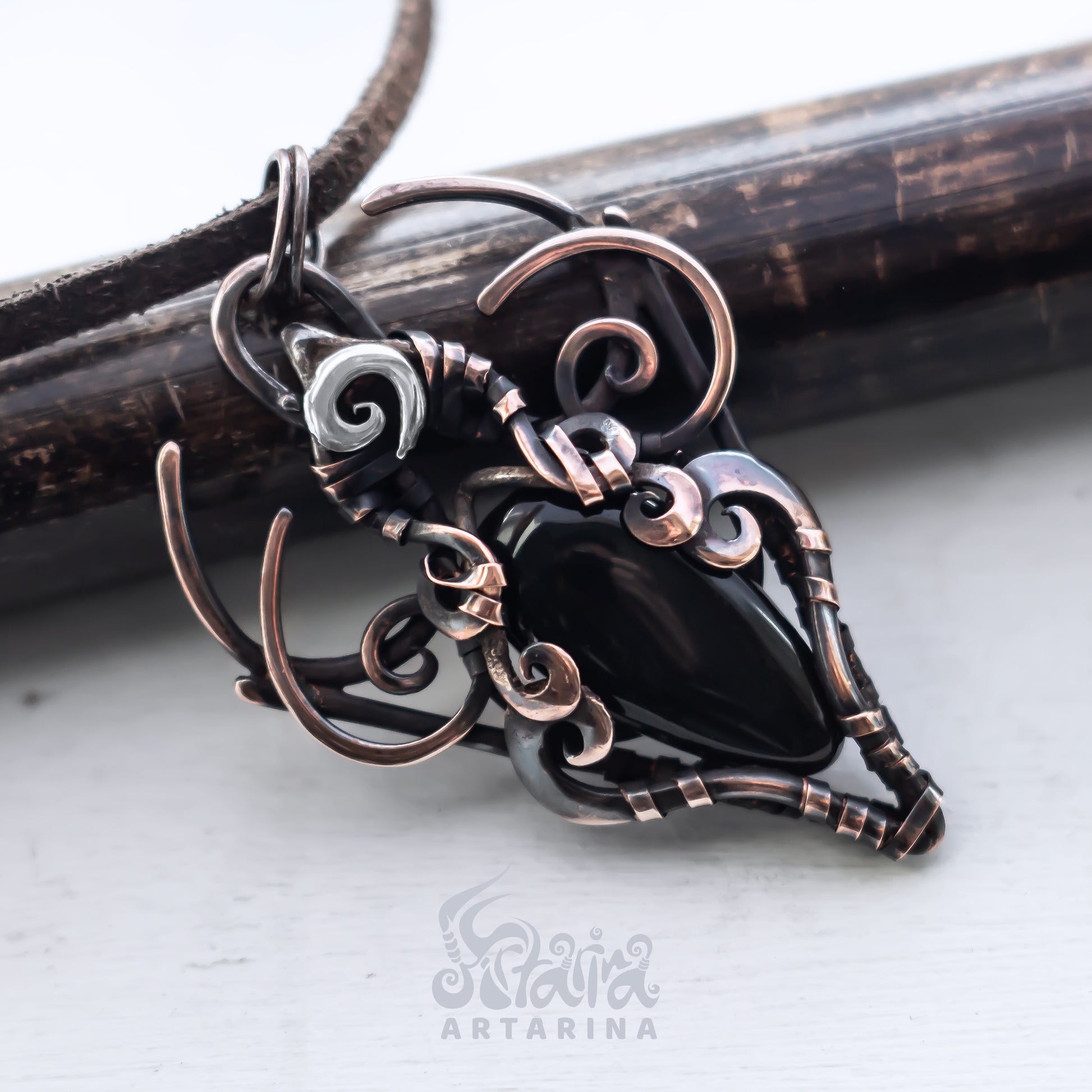 Ornate copper and silver pendant on a white background with 'Artarina' branding.