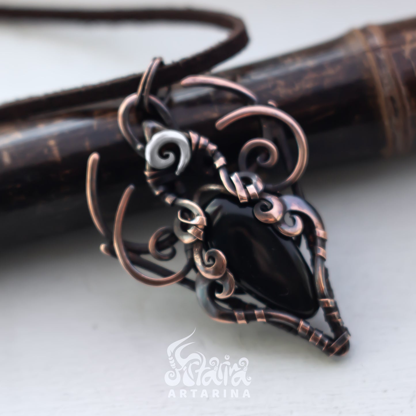 Copper and black stone pendant on a white background with 'Artarina' branding.